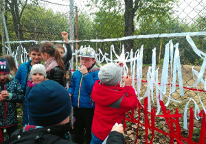 uczniowie wiążą białe i czerwone wstążki na siatce ogrodzenia